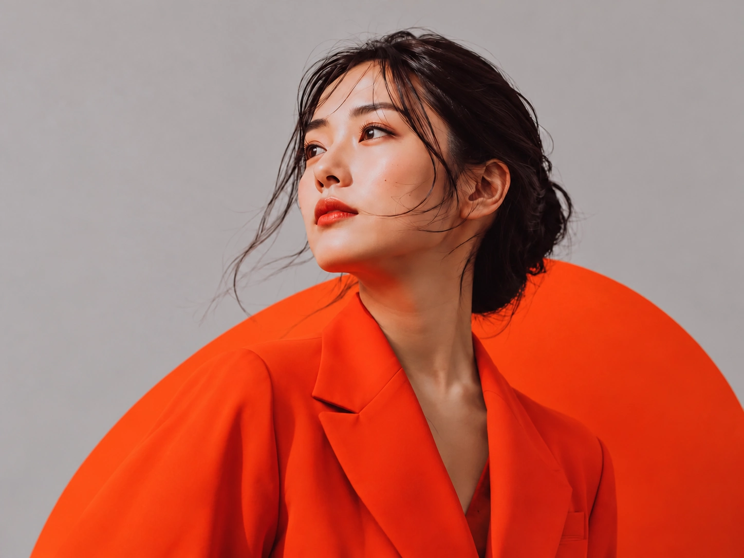 Portrait of Hinata Sakai in an orange suit against a grey backdrop